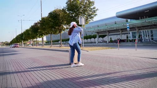 Cheerful Young Woman in Summer Cap and Sunglasses Walking Near Airport with Suitcase. Happy Lady