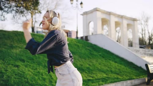 Young Woman Enjoys Music While Dancing Outdoors in a Park During a Sunny Day Near Classic