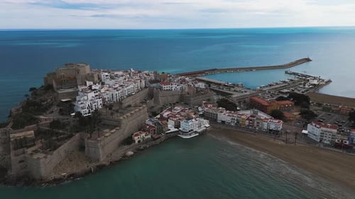 Drone circles cliffs with waves along fortress walls