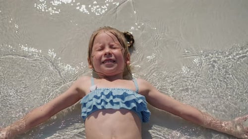 Little Girl in Swimsuit Waves Hands in Surfline on Beach