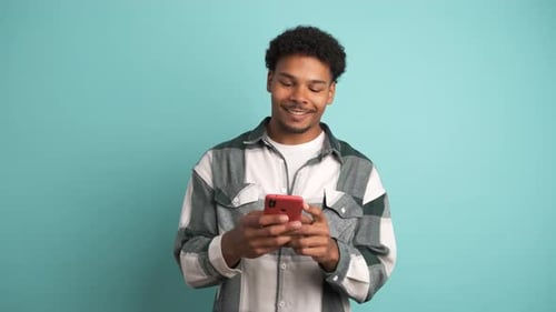 Cheerful Young Man Using Smartphone in Blue Studio