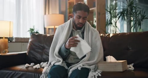 Ill Man Blowing Nose on Couch at Home
