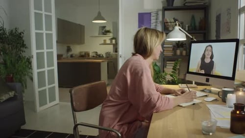 Woman on Video Call Taking Notes at Desk