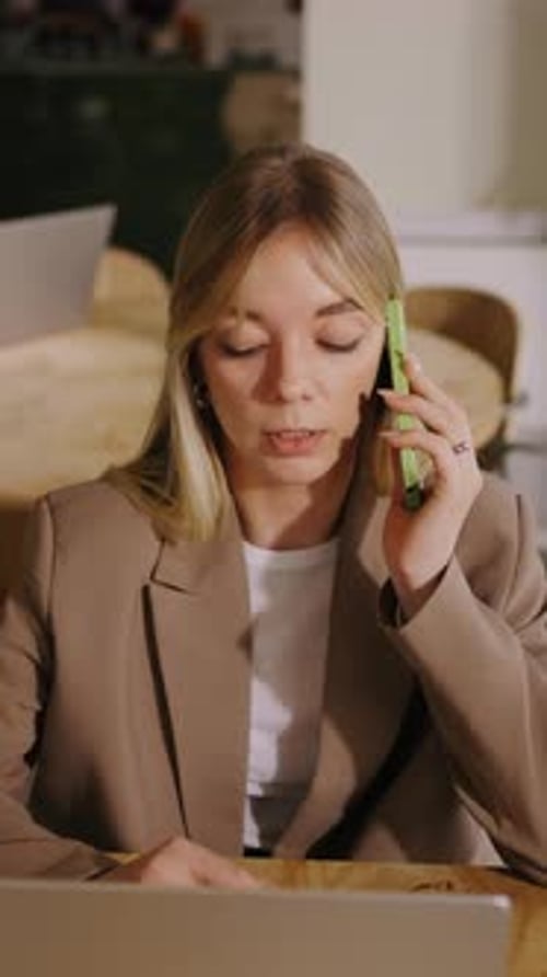 Woman in blazer talking on phone while using laptop