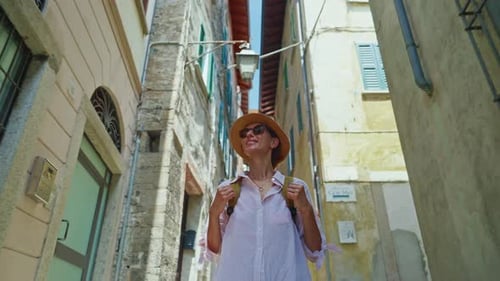Young Attractive Woman Tourist in a Hat with a Backpack Wanders the Street of the Old City While