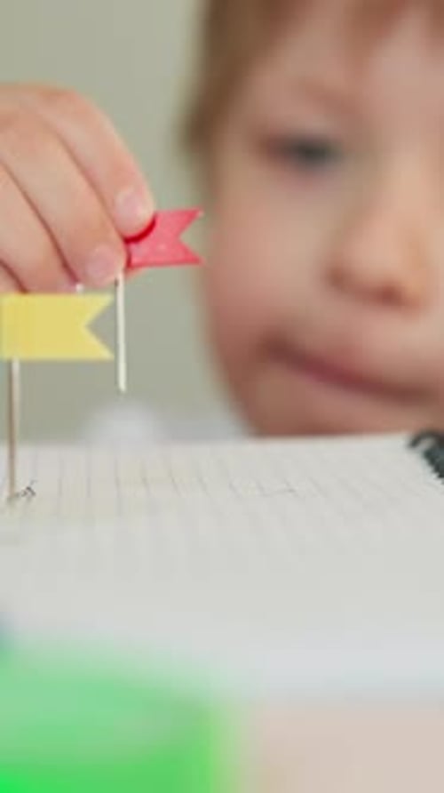 Toddler Boy Replaces Pin with Small Red Tag on Notebook