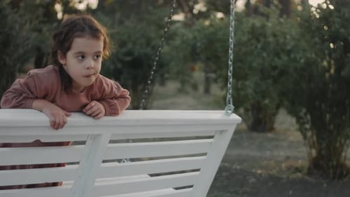 Little 5 Yo Girl Having Fun on a White Swing in a Quiet Treelined Park Background Preschooler