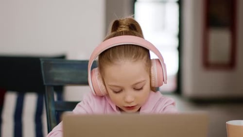 Girl Wearing Headphones Uses Laptop at Table