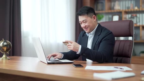 Happy asian business man shopping online customer paying by bank credit card sitting in a modern