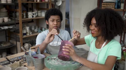 African woman and man make earth ware at workshop.