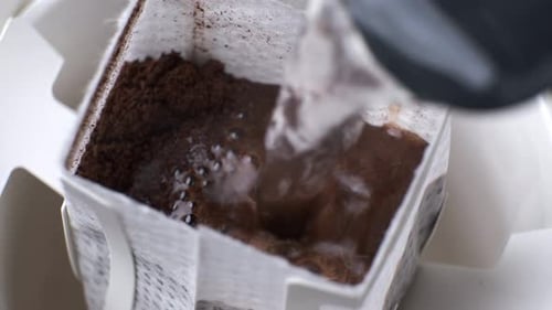 Pour boiling water into drip bag coffee, close-up.