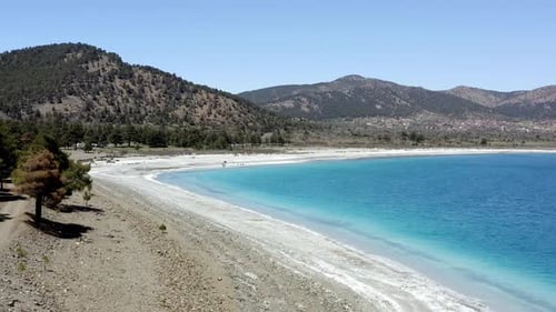 Descending drone to hills over white beach and turquoise water of Lake Salda