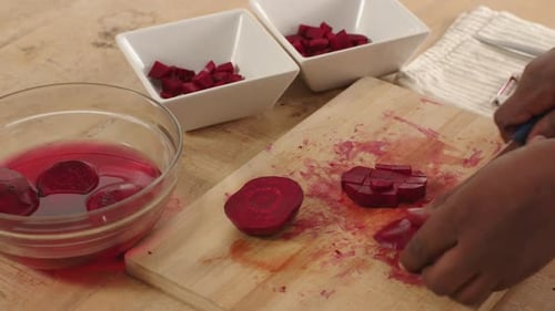 African American man in 30s placing halved beet, dicing with blue knife, filling bowls, copy space