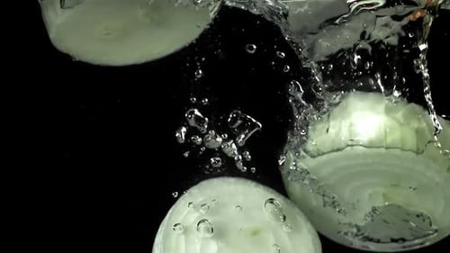 Sliced Onions Dropping into Water on Black Background