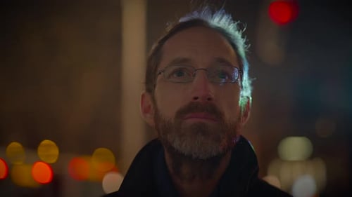 Man in Glasses at Night with Passing Lights