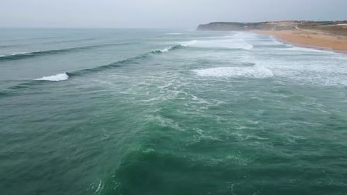 Dramatic aerial panorama of foamy waves crashing on sandy beach under gloomy sky