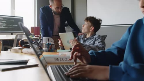 Diversos escolares trabajan en proyectos con computadoras portátiles y tabletas en la clase de programación
