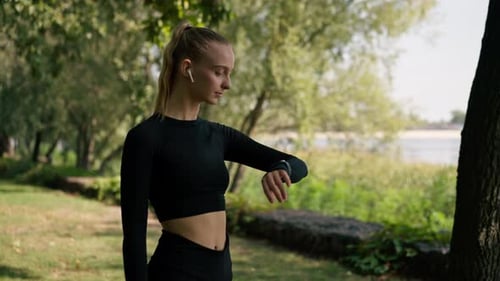 Sporty girl during a morning jog in the park looks at the sports watch on her hand to determine