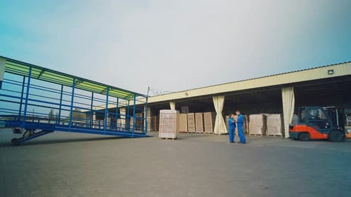 Warehouse Workers Discussing Logistics with Forklift Moving Pallets