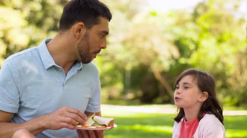 Family eats sandwiches during bright day picnic in park