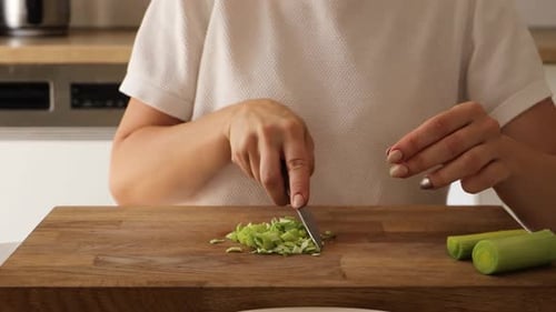 Woman Cutting Leeks on Wooden Board in Kitchen