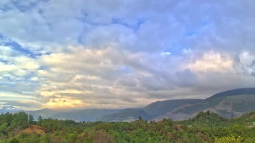Clouds are Flying in the Sky Above Green Valley with Hills and Mountains Filmed in Timelapse