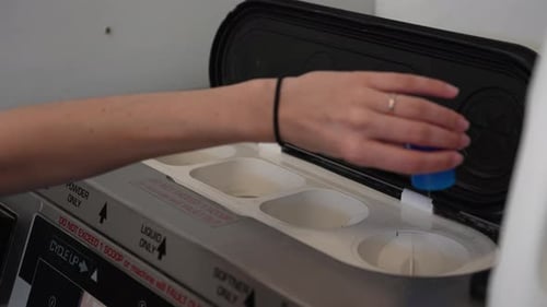 Female hand pours liquid laundry detergent into top of washing in laundromat