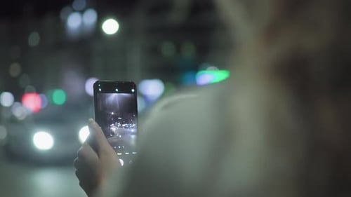Rear View of Woman Taking Photo of Night Traffic with Smartphone and City Lights