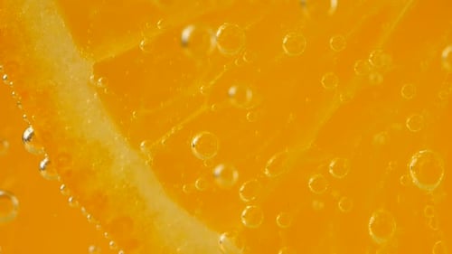 Eine Scheibe reifer Orange im Wasser sprudelt auf einem orangefarbenen Hintergrund.