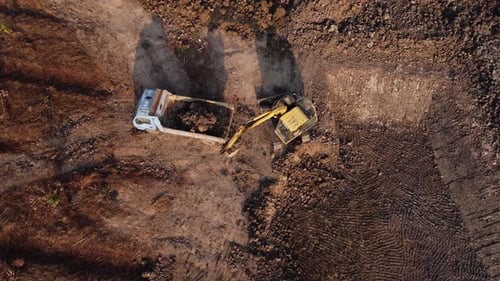Aerial view of a wheel loader excavator with a backhoe loading sand into a heavy earthmover