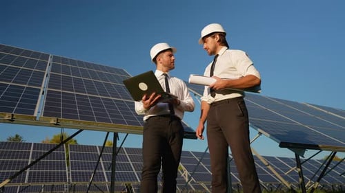 Two Engineers in Helmets and Formal Attire Analyze Data on a Laptop and Discuss the Performance