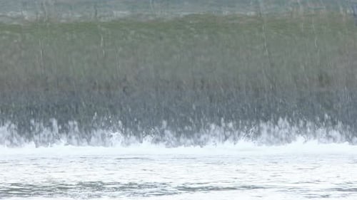 Base of low concrete river weir with water flowing smoothly over
