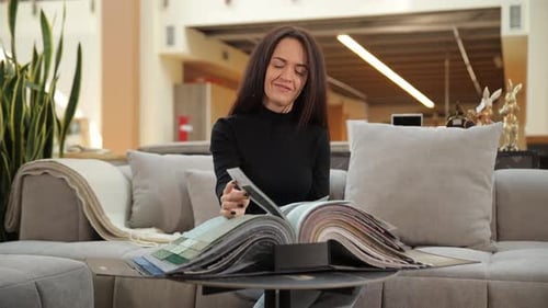 Woman Sitting on Modern Sofa Browsing Home Interior Catalog in Furniture Showroom