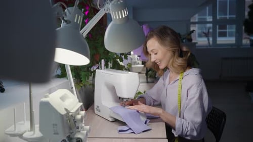 A Seamstress Woman Works at a Sewing Machine in a Cozy Workshop Fulfills Orders for a New Collection