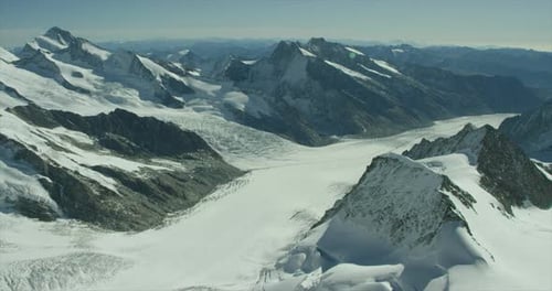 High alpine glacier surrounded by snow covered mountain tops under blue sky