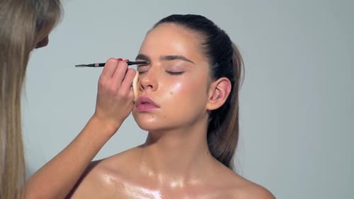 Linda jovem recebendo maquiagem de sobrancelhas Maquiadora aplica maquiagem com pincel cosmético Beauty