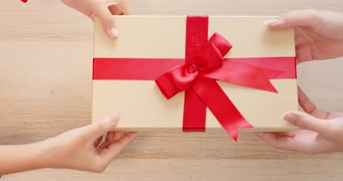 Hands Passing Beautiful Gift Box with a Red Ribbon