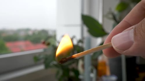 Holding a burning match stick indoors by a window.