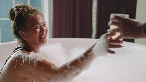 Woman Enjoying Bubble Bath Takes Glass of Wine