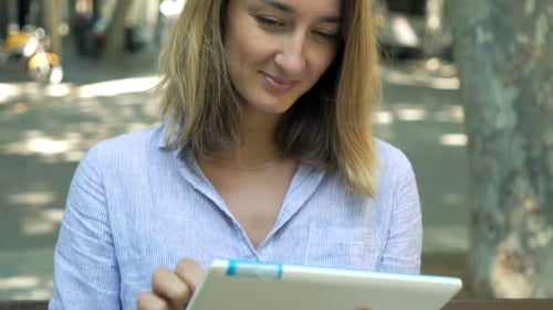 Young Woman with Tablet Computer Sitting on Bench in City 30s