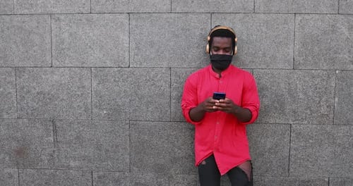 Man Using Smartphone with Headphones Standing by Wall