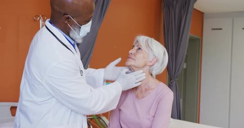 African american male doctor examining the neck of senior caucasian female patient at hospital