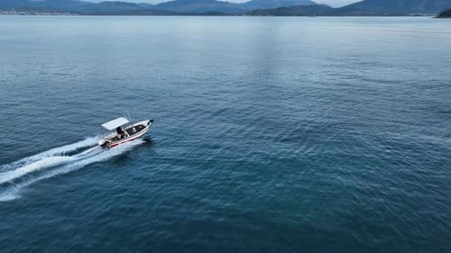 Speedboat Motorboat Cruising Fast on Blue Ionian Sea, Drone Tracking Shot with Mountains and Sunset