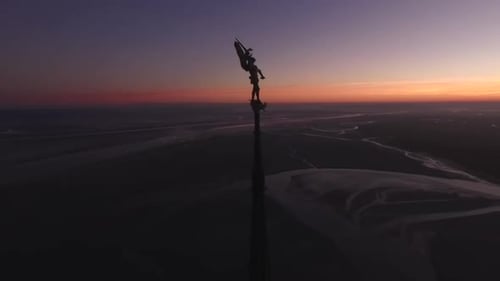 Silhouette of statue on top of Abbey spire and view of bay at dusk, Mont Saint-Michel in Normandy, F