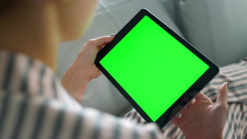 Woman in pajamas holds mockup tablet checking chroma key screen at home weekend