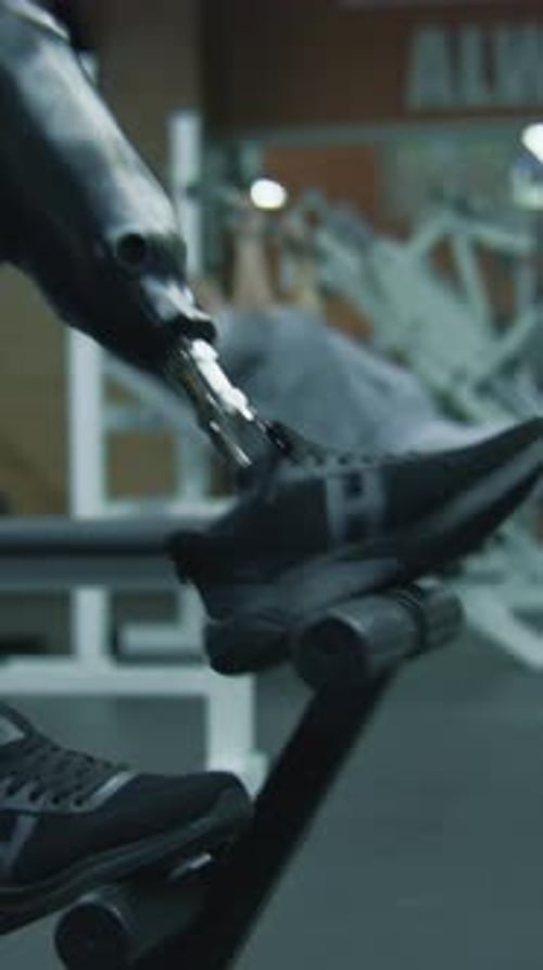 Sportsman with Prosthetic Leg Exercises on Workout Machine in Gym