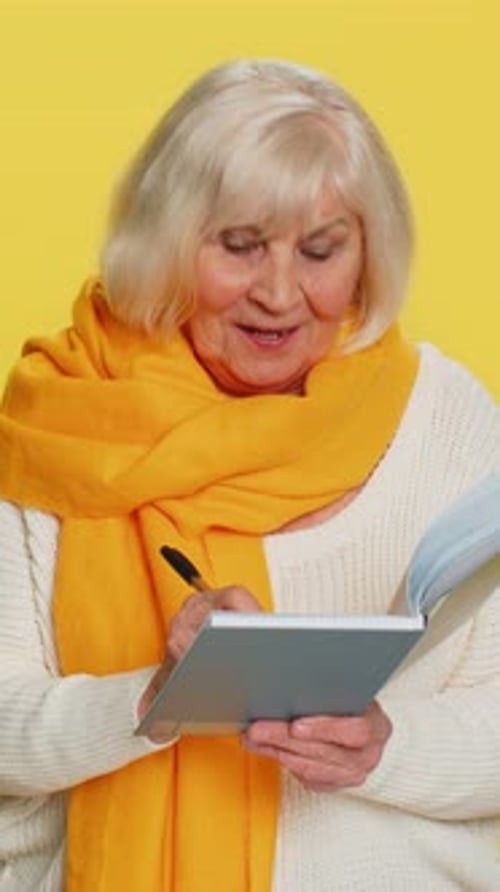 Smiling Senior Woman Writing in Notebook on Yellow