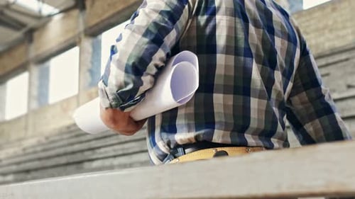Construction worker with blueprint walking at building site.