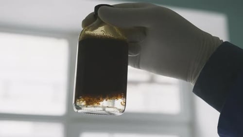 Hand Holding Vial with Dark Liquid