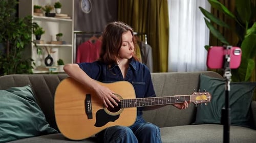 Young Woman Recording Guitar Lesson with Phone at Home